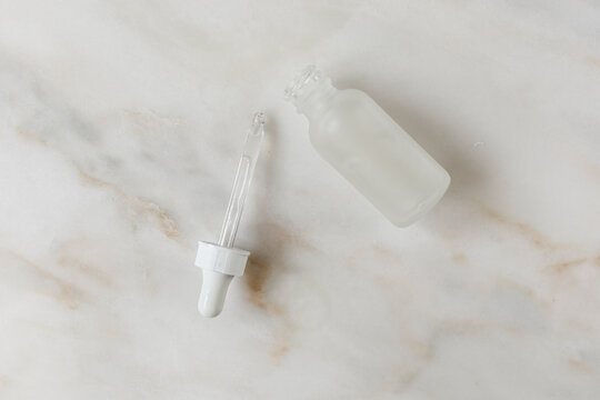 dropper bottle frosted white on marble vanity top, flat lay, top view