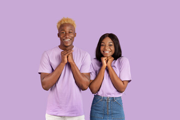 Excited black couple anticipating something wonderful, making wish, begging or praying over violet studio background