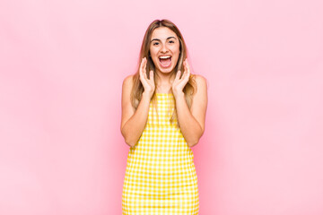 blonde woman feeling shocked and excited, laughing, amazed and happy because of an unexpected...