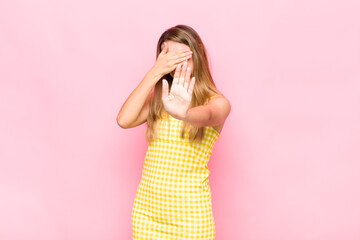 blonde woman covering face with hand and putting other hand up front to stop camera, refusing...