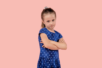 A disgruntled angry girl is upset and looks angrily at the camera in a blue dress. Pink isolated background.
