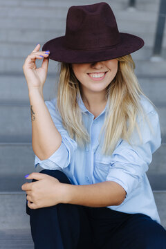 Smiling blonde hiding her eyes behind trendy hat