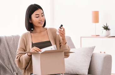 Happy asian lady unpacking parcel with beauty box