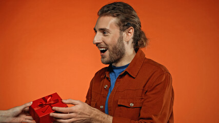 happy young man receiving wrapped present on orange