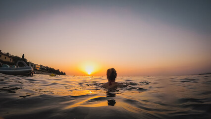 Back view of a woman swimming towards the sunset in the sea. Romantic swim in the late afternoon