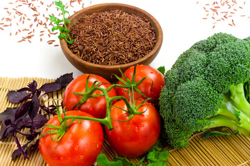 Red wild rice in wooden bowl and fresh vegetables on sushi bamboo mat. Organic food concept. Eastern culinary ingredients