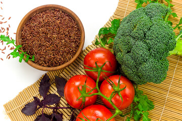 Red wild rice in wooden bowl and fresh vegetables on sushi bamboo mat. Organic food concept. Eastern culinary ingredients