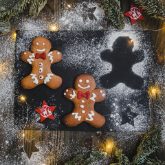 gingerbread men.
Three ginger men, one big, two small. Against the backdrop of snow made of flour, fir branches and a wooden background. Homemade cookies, Christmas baked goods. December traditions