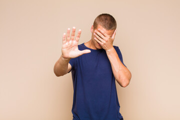 blonde  man covering face with hand and putting other hand up front to stop camera, refusing photos...