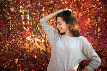 A very happy young girl stands in the autumn forest and smiles. The foliage behind it is bright red.