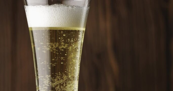 Cold beer is slowly poured into a glass on a dark wooden background, there is a lot of foam and bubbles in the glass. Slow motion. Beer is pouring into a glass isolated on a wooden background. 