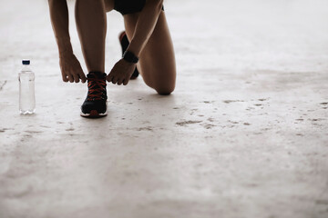 Muscular lady in sports uniform and fitness tracker ties shoelaces on sneakers on floor, free...