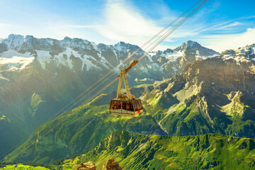 Cable car from Murren to Birg and Schilthorn summit above cliffs, rocky mountains and valleys with lakes and rivers. Snow-capped peaks of Bernese Prealps, Canton of Bern, Switzerland. Summer season.