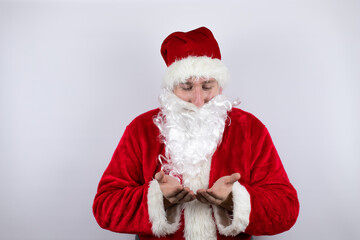 Man dressed as Santa Claus standing over isolated white background Smiling with hands palms together receiving or giving gesture. Hold and protection