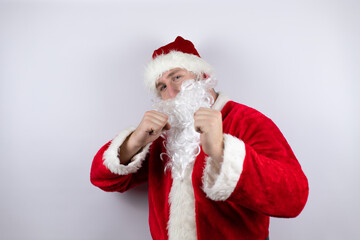 Fototapeta na wymiar Man dressed as Santa Claus standing over isolated white background Punching fist to fight, aggressive and angry attack, threat and violence