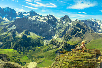 Mountain panorama of the Eiger, Monch and Jungfrau UNESCO World Heritage Site and over 200 peaks. Tourist woman relaxing after hiking at Schilthorn viewpoint in Bernese Oberland, Jungfrau Region.