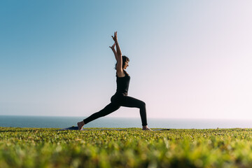 Mujer joven estira sus brazos arriba practicando yoga al atardecer.