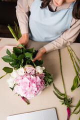 Cropped view of female florist in apron composing bouquet on desk with stalks