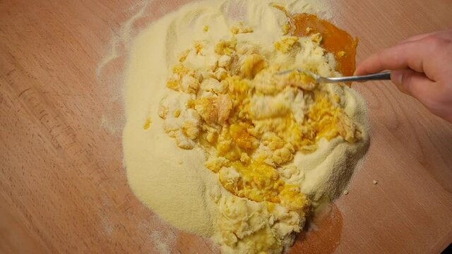 Using a fork on a wooden table, mix semolina and egg
