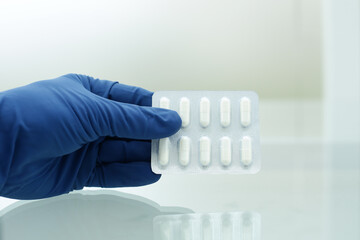 A hand in a blue medical glove holds a package of white pills