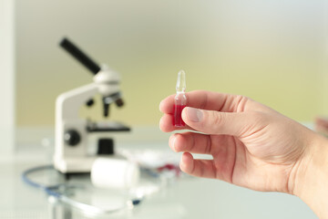 Doctor's hand holding a vaccine in his hands on the background of a glass table with medicines and a microscope