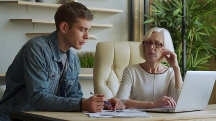 Elderly businesswoman communicates with middle aged businessman, discussing working issues, look at laptop screen, management distributes tasks for employee - Powered by Adobe
