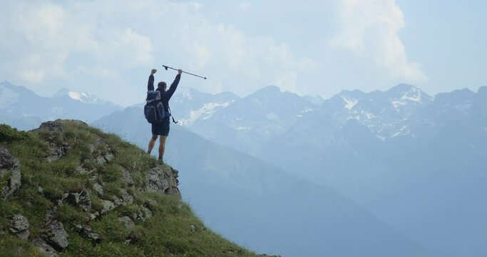A man stands on the top of a mountain. A man raises his hands a winner after climbing the mountain. Joy of victory