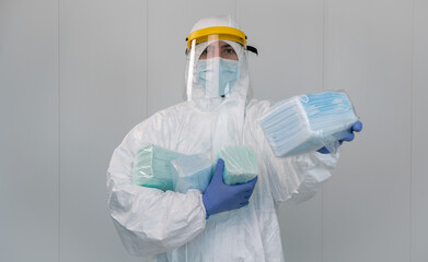 Male nurse wears protective suit shows a pack of medical masks. Coronavirus