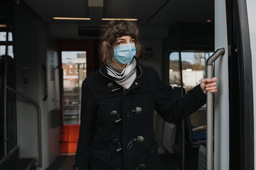 Fototapeta na wymiar Coronavirus, COVID-19. Young modern woman with medical face mask to protect against the coronavirus while getting in the train on the subway platform. Mouth protection at the train station.