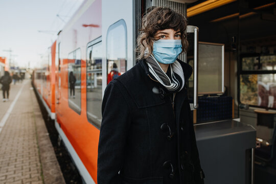 Young german woman with medical face mask to protect against the coronavirus while waiting for the train on the subway platform. Mouth protection obligation at the train station. Pandemic Germany.