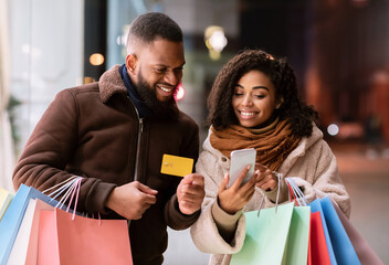 Portrait of happy black couple using smartphone holding credit card
