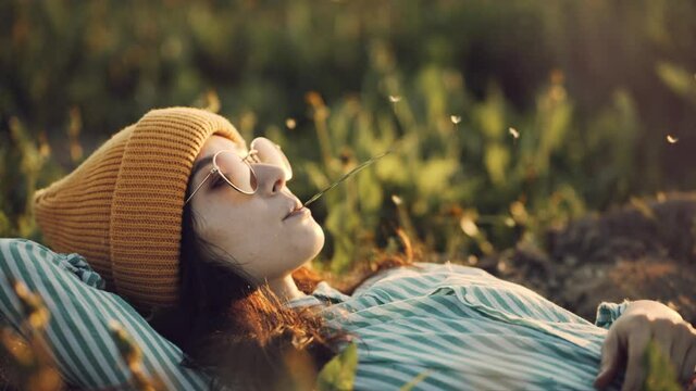Social distancing and solo activity. Beautiful young girl on self isolation laying on sunset field chewing grass enjoying her loneliness. Hipster japanese portrait in stylish sunglasses and yellow cap