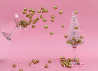 Golden decorative balls splash from the champagne glass on the Christmas tree. Celebration Christmas and New Year minimalistic abstract concept. Cheers with champagne. 