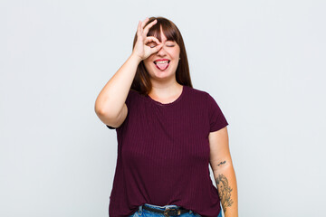 overweight woman smiling happily with funny face, joking and looking through peephole, spying on...