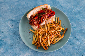 plant-based food, vegan hot dog with vegetable sausage topped with sauteed red pepper and onion with a side of french fries