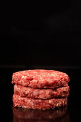 pile of raw burgers on black background