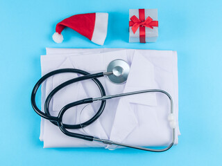 Stethoscope, white robe, gift and santa hat on a blue background, top view close-up.