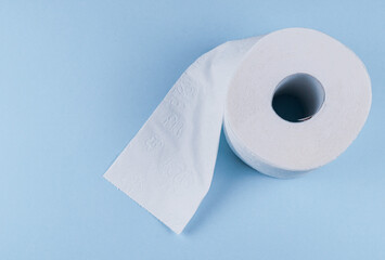 Toilet paper lies on the right against a blue background with space for text on the left, top view close-up.