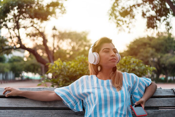 Young woman enjoys music through the headphones in the park