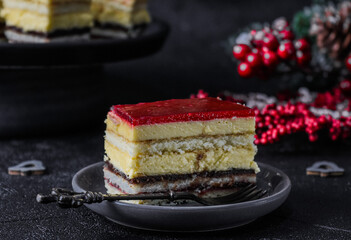 piece of cake on a plate.
A slice of strawberry-chocolate cake in a plate with a fork and christmas decor on a black background, close-up side view.