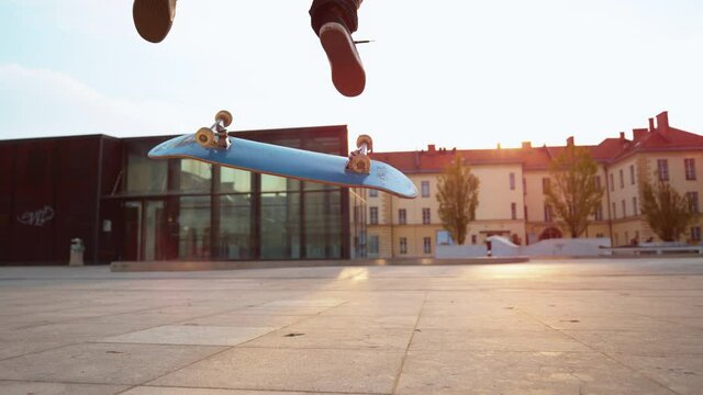 SLOW MOTION TIME WARP, CLOSE UP, LOW ANGLE, LENS FLARE, DOF: Unrecognizable skater does a flip trick while riding around a square. Cinematic shot of a skateboarder doing a nollie kickflip at sunset.