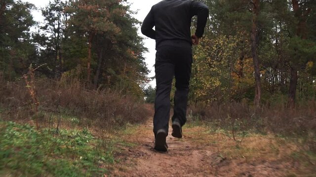 Slow motion. Men's legs are running. A man is running through the forest, a close-up sneakers. Concept sports, jogging, running. The sportsman goes in for sports and runs in the summer park. Close-up