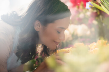 Side view of smiling female florist with closed eyes smelling flower on blurred foreground