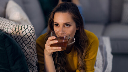 Young pretty woman drinks a cup of tea while lying on the couch - home shooting