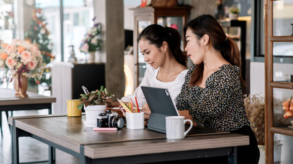 Two beautiful asian woman working together in a coffee shop with a digital tablet.