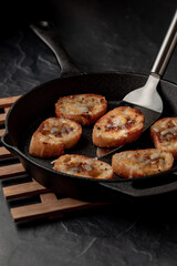 A frypan filled with fried cheese bread rounds against a dark background.