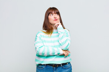 overweight woman with a concentrated look, wondering with a doubtful expression, looking up and to...