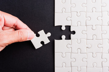Top view flat lay of hand-holding last piece white paper jigsaw puzzle game last pieces put to...