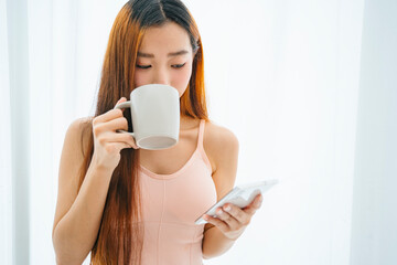Beautiful asian woman holding cup of coffee and using smartphone.