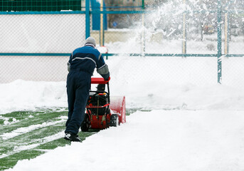 Man using a snow blower to remove large amounts of snow on football field. Man cleans snow with a...